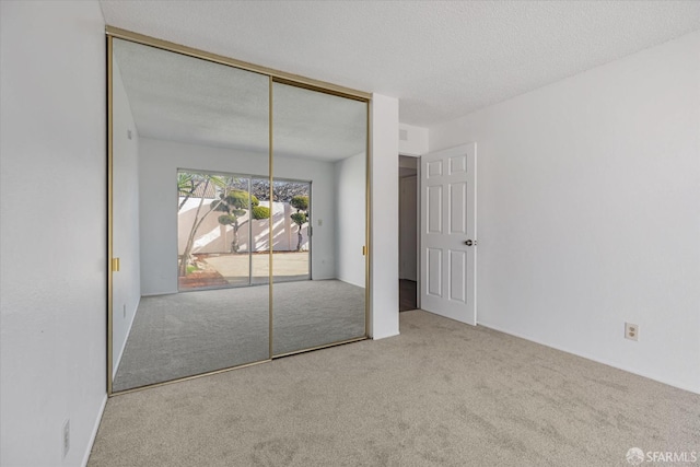 unfurnished bedroom featuring a textured ceiling, a closet, and light carpet