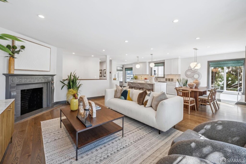 living room with wood finished floors, a fireplace with raised hearth, and recessed lighting
