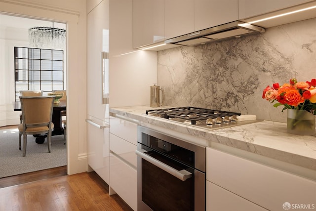 kitchen featuring light wood-style flooring, decorative backsplash, appliances with stainless steel finishes, white cabinetry, and under cabinet range hood