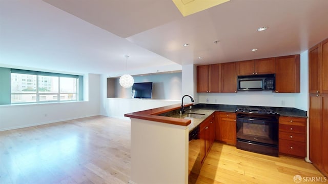 kitchen featuring light hardwood / wood-style flooring, kitchen peninsula, sink, black appliances, and decorative light fixtures