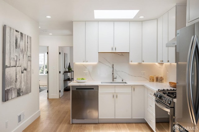 69 Lobos St, San Francisco, CA 94112 - kitchen featuring appliances with stainless steel finishes, a skylight, light countertops, light wood-style floors, and white cabinetry