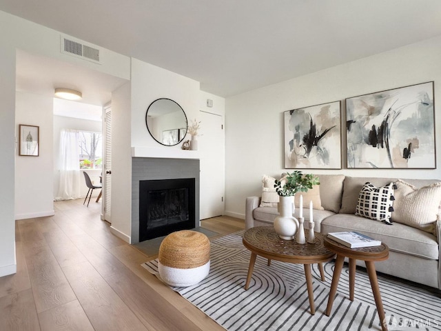living area featuring baseboards, a fireplace with flush hearth, visible vents, and wood finished floors