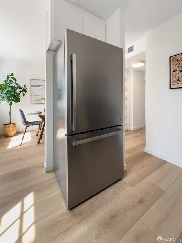 kitchen featuring freestanding refrigerator, light wood-style floors, visible vents, and white cabinetry