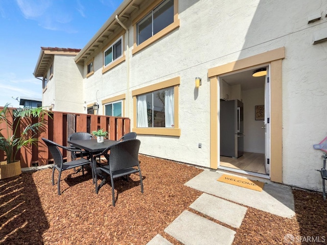 back of property featuring outdoor dining area, fence, and stucco siding