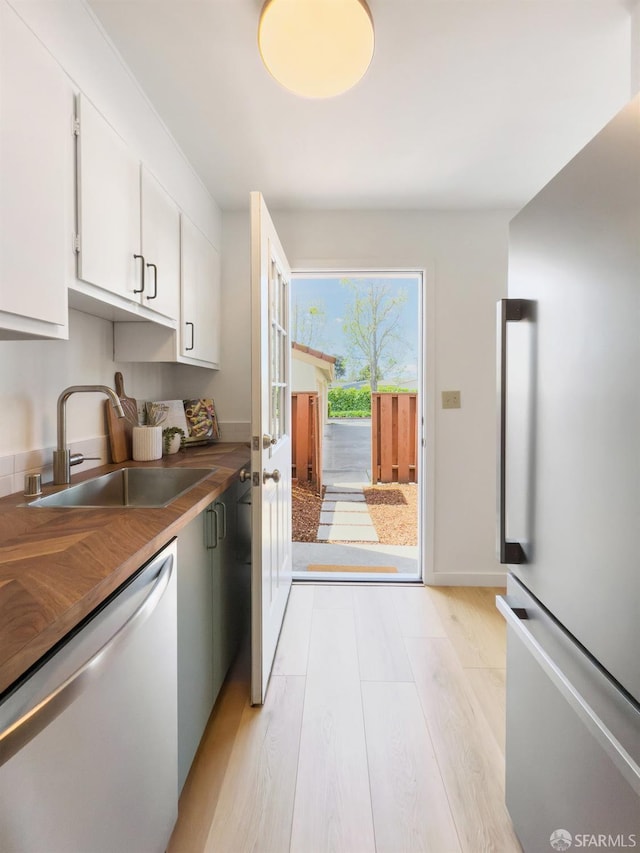 kitchen with a sink, freestanding refrigerator, dishwashing machine, white cabinets, and light wood-style floors