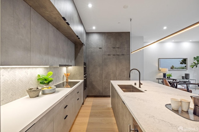 kitchen with tasteful backsplash, sink, light wood-type flooring, light stone countertops, and black electric cooktop