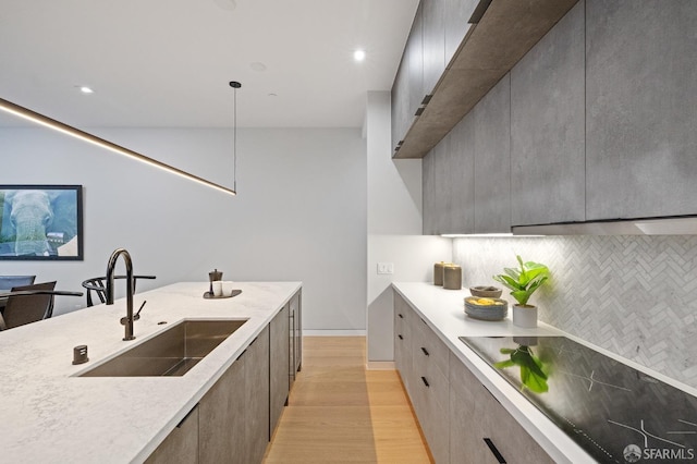 kitchen featuring pendant lighting, sink, backsplash, light hardwood / wood-style floors, and black electric cooktop