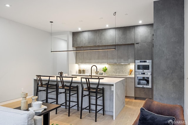 kitchen with decorative backsplash, decorative light fixtures, an island with sink, and light hardwood / wood-style flooring