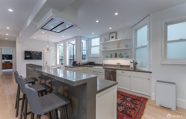 kitchen featuring an inviting chandelier, a breakfast bar, dark countertops, stainless steel dishwasher, and light wood-type flooring