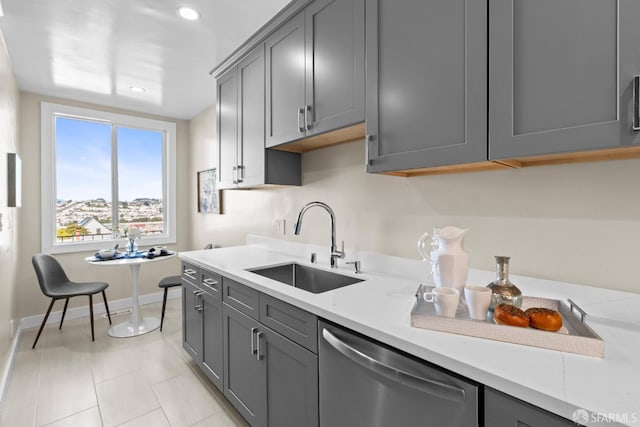 kitchen with light stone countertops, sink, stainless steel dishwasher, and gray cabinetry