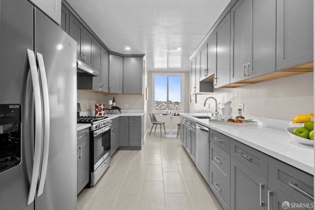 kitchen with gray cabinetry, sink, stainless steel appliances, and light stone countertops