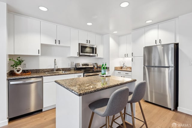 kitchen with light hardwood / wood-style floors, appliances with stainless steel finishes, sink, a kitchen island, and white cabinets