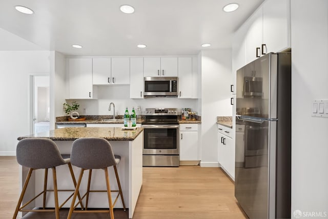 kitchen with sink, light wood-type flooring, white cabinets, dark stone countertops, and stainless steel appliances