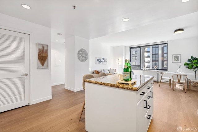 kitchen with a breakfast bar, white cabinets, light wood-type flooring, and light stone counters