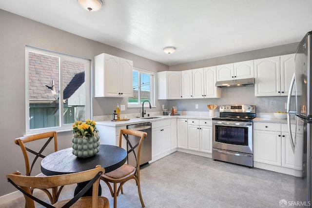 kitchen with white cabinets, stainless steel appliances, light countertops, under cabinet range hood, and a sink