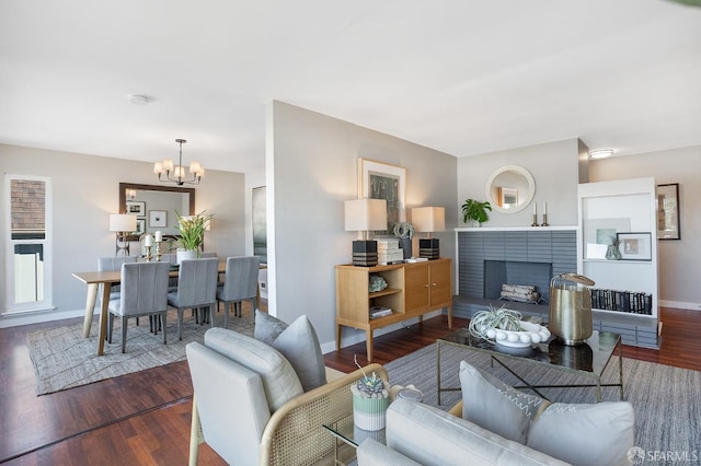 living room featuring baseboards, a fireplace, wood finished floors, and a notable chandelier