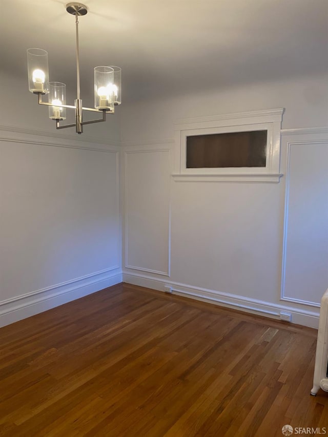 spare room with a chandelier and dark wood-type flooring