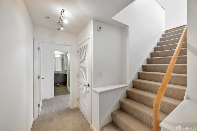 stairway featuring carpet floors, rail lighting, and baseboards