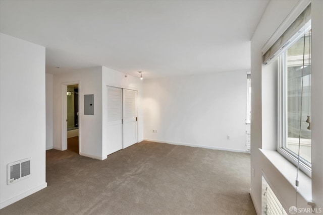 carpeted spare room featuring baseboards, a healthy amount of sunlight, visible vents, and electric panel