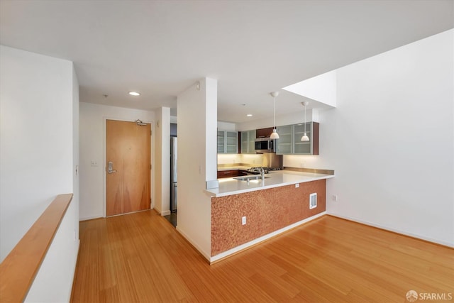 kitchen featuring light countertops, light wood-style flooring, glass insert cabinets, appliances with stainless steel finishes, and a sink