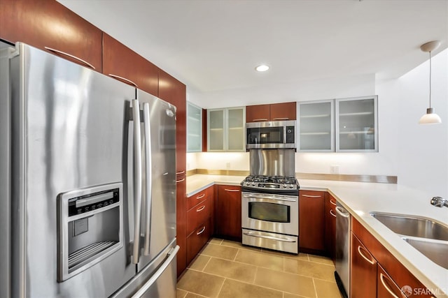 kitchen featuring a sink, light countertops, appliances with stainless steel finishes, glass insert cabinets, and pendant lighting