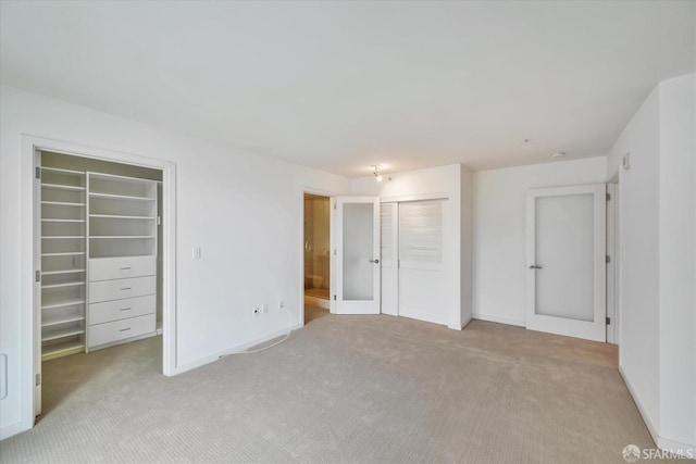 unfurnished bedroom with light carpet, a spacious closet, and baseboards