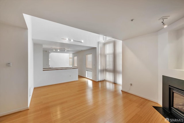 unfurnished living room featuring baseboards, light wood finished floors, a fireplace with flush hearth, and track lighting