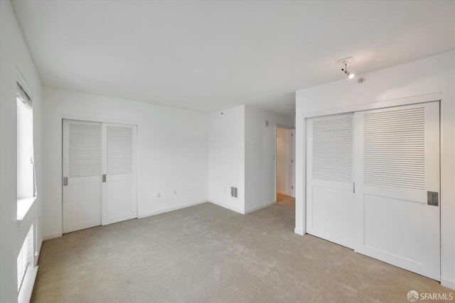 unfurnished bedroom with baseboards, two closets, visible vents, and light colored carpet