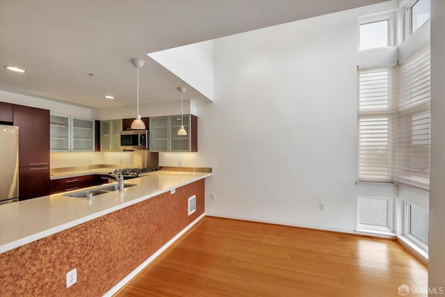 kitchen with appliances with stainless steel finishes, glass insert cabinets, wood finished floors, light countertops, and a sink