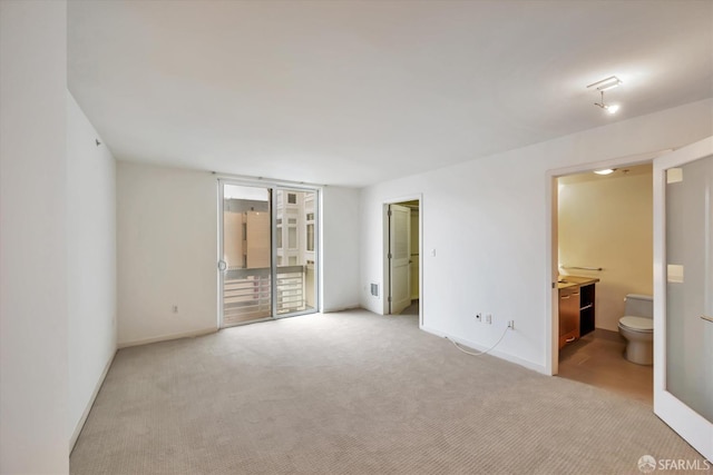 unfurnished bedroom featuring light carpet, access to exterior, baseboards, and ensuite bathroom