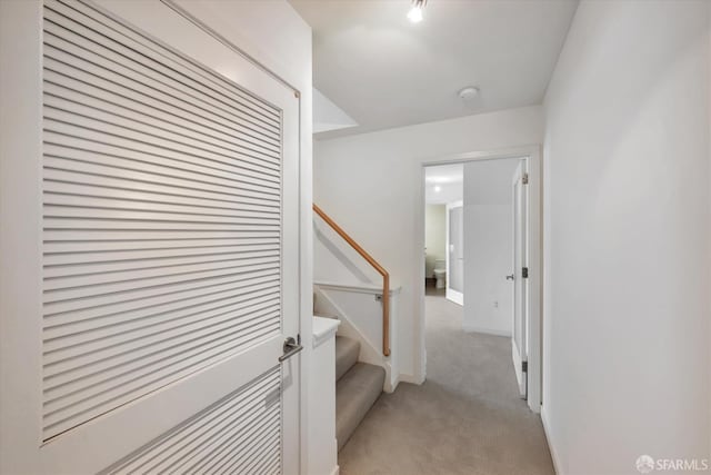 hallway featuring stairs, baseboards, and light colored carpet