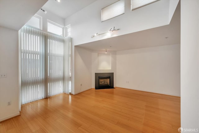 unfurnished living room with a fireplace with flush hearth, baseboards, and light wood finished floors