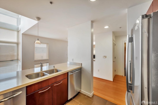 kitchen with a sink, hanging light fixtures, appliances with stainless steel finishes, light countertops, and reddish brown cabinets