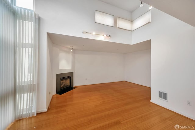 unfurnished living room featuring visible vents, baseboards, a towering ceiling, a fireplace with flush hearth, and light wood-style floors