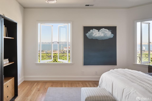 bedroom with crown molding, light hardwood / wood-style floors, and a water view