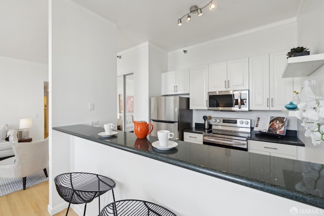 355 Buena Vista E Avenue 605W, San Francisco, CA 94117 - kitchen featuring white cabinets, appliances with stainless steel finishes, light wood-style floors, dark stone counters, and a kitchen bar