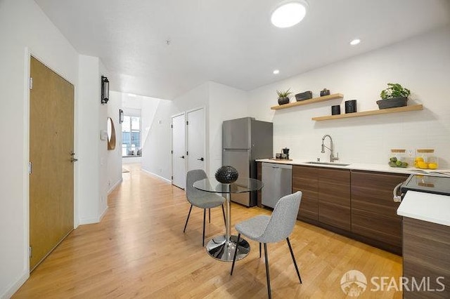 kitchen with tasteful backsplash, appliances with stainless steel finishes, sink, and light wood-type flooring