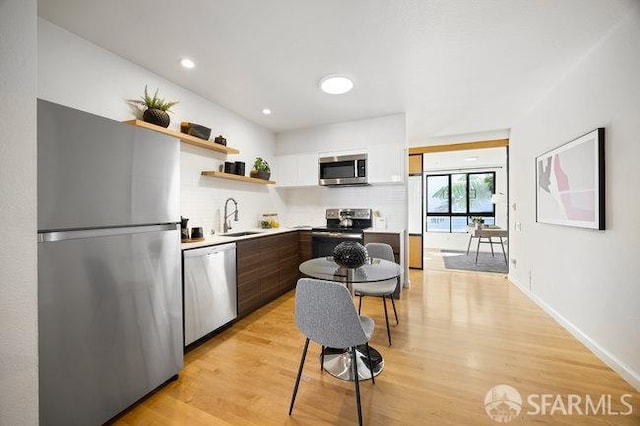 kitchen with dark brown cabinetry, sink, appliances with stainless steel finishes, light hardwood / wood-style floors, and white cabinets