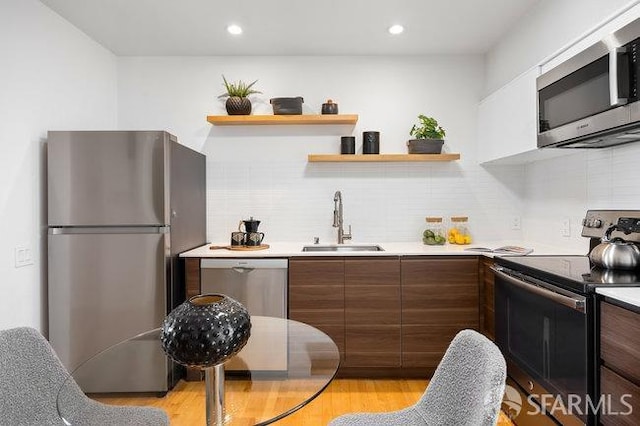 kitchen with sink, decorative backsplash, light hardwood / wood-style flooring, and appliances with stainless steel finishes