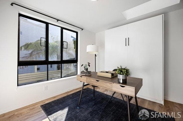 home office with hardwood / wood-style flooring and a skylight