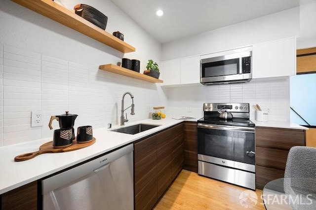 kitchen featuring sink, light hardwood / wood-style flooring, appliances with stainless steel finishes, white cabinetry, and dark brown cabinets