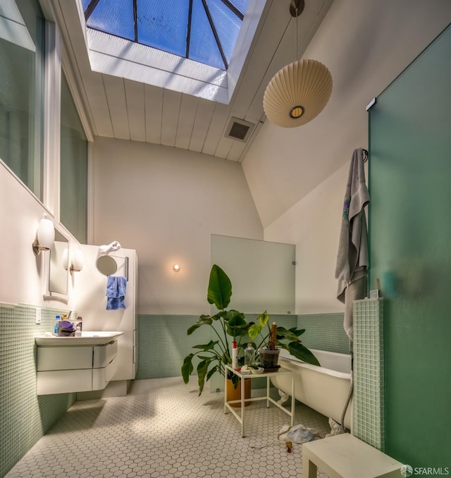 bathroom with tile walls, vanity, and vaulted ceiling with skylight