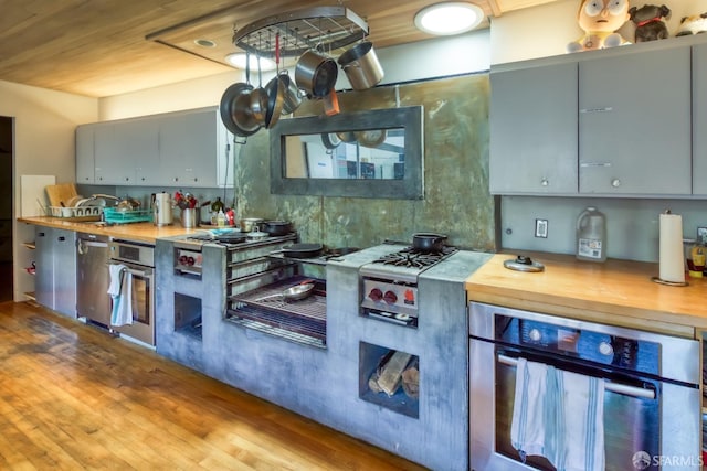 kitchen with gray cabinetry, oven, light hardwood / wood-style flooring, and wooden counters