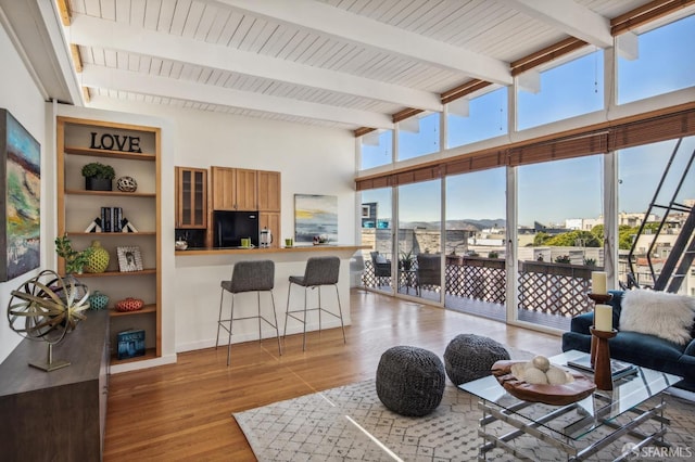 living area with light wood-style floors, beam ceiling, a high ceiling, and a wealth of natural light