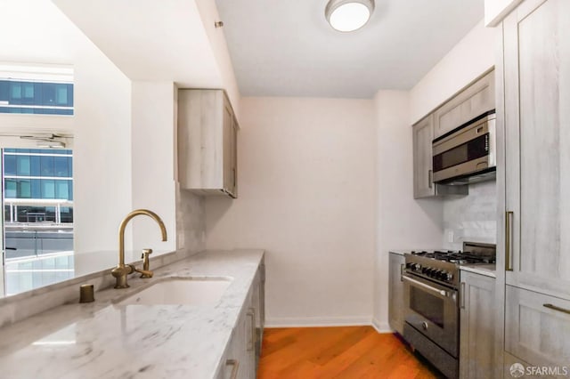 kitchen with light stone counters, light wood-style flooring, stainless steel appliances, a sink, and baseboards