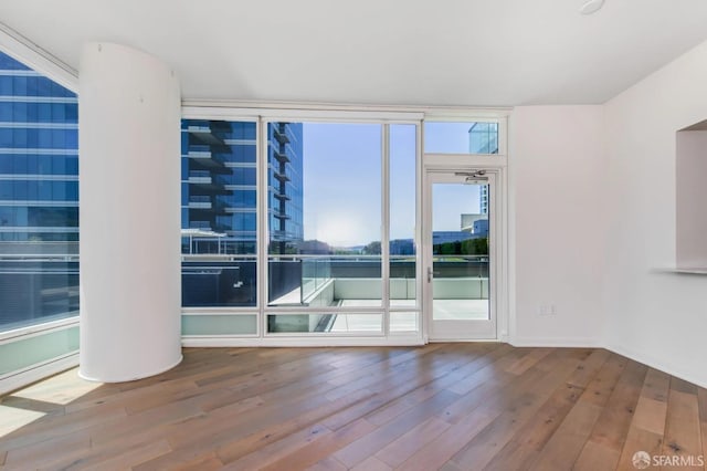 spare room featuring a wall of windows, wood finished floors, and baseboards