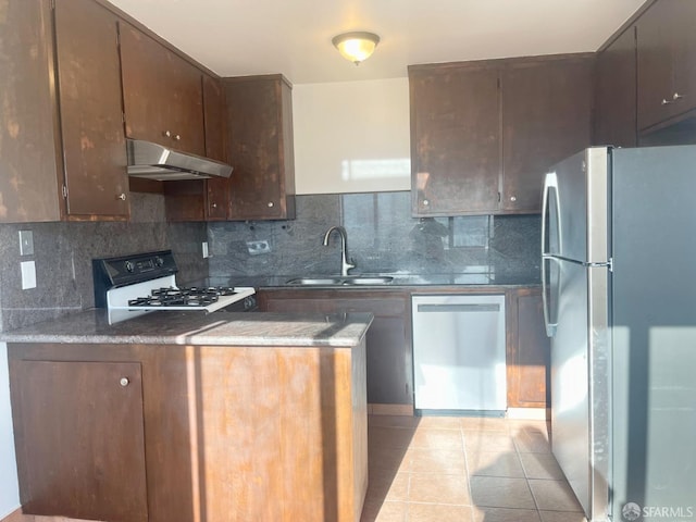 kitchen with light tile patterned flooring, under cabinet range hood, stainless steel appliances, a sink, and dark countertops