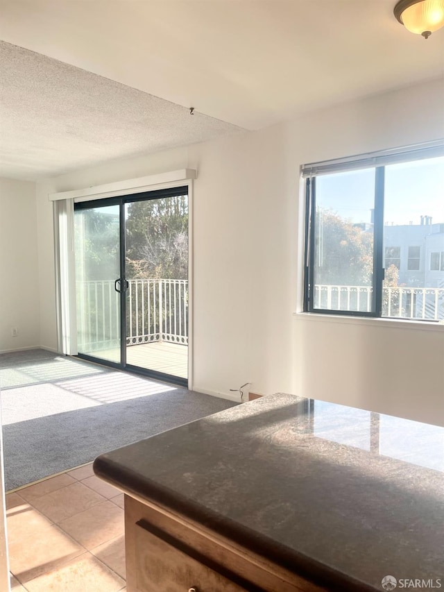 empty room featuring light colored carpet, a textured ceiling, and light tile patterned flooring