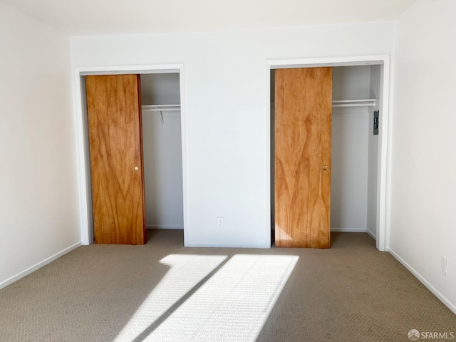 unfurnished bedroom featuring carpet floors, baseboards, and two closets