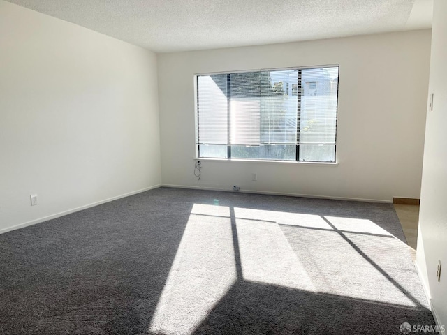 unfurnished room with dark colored carpet, a textured ceiling, and baseboards